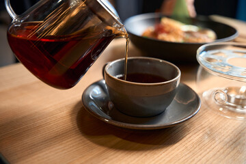 Close-up view person pouring freshly brewed loosed leaves tea into cup