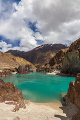 Landscape of sandy beaches amidst Jagged Mountain rocks and clear green water In Ladakh.
