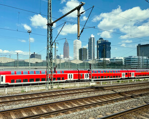 red and white passenger train on railway tracks in front of a cityscape with modern high-rise buildings © Jarama