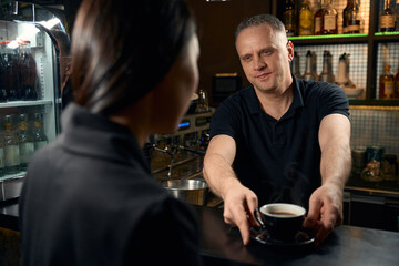 Handsome barman treating brunette woman with cup of freshy brewed coffee