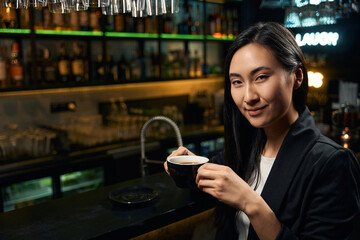 Smiling Asian woman drinking fragrant black coffee in favorite cafe