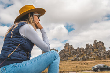 A woman wearing a yellow hat and blue jeans is sitting on a rock in a Huayllay Stone Forest, Peru.