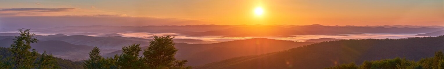 A panorama of a mountain valley in the morning mist. Picturesque dawn in the summer mountains. Warm sunlight
