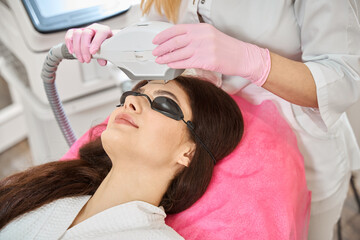 Young woman undergoing intense pulsed light therapy done by beautician