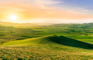 beautiful green valley with green fields with green spring grass with nive hills and mountains and scrnic colorful cloudy sunset on background of landscape