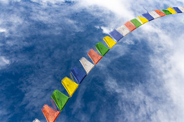 Colorful Tibetan prayer flags attached to a string flying in air against blue sky with clouds   
