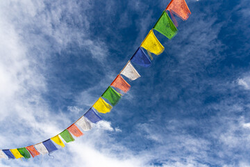 Colorful Tibetan prayer flags attached to a string flying in air against blue sky with clouds   