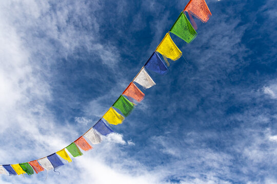 Colorful Tibetan prayer flags attached to a string flying in air against blue sky with clouds   