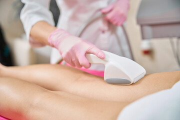 Cosmetician conducting skin tightening treatment on patient upper leg