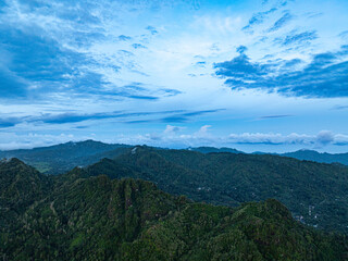 Fototapeta premium Aerial view Kabut Pelangi Waterfall in East Java. The waterfall stream flows into the mountain gorge in a long path.Above is the residence of the villagers. Abundance of forests on the green mountain.