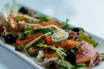 Salad with cabbage, cucumber, egg, onion, tuna and olive oil on a white saucer on a white background