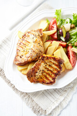 Grilled Steaks with french fries and fresh salad. Bright wooden background.	