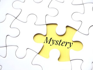 A white puzzle with a single yellow gap with the word 'mystery' written inside. Mystery or enigma...