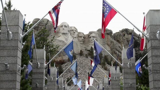 Mount Rushmore monument with the Avenue of Flags in the foreground, South Dakota. The carved faces of the four presidents are standing majestically against the sky. The flags add a patriotic touch.