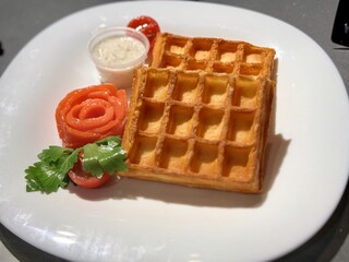 A plate with crispy waffles, smoked salmon, sauce, and garnished with herbs. Perfect for breakfast or brunch. Close-up