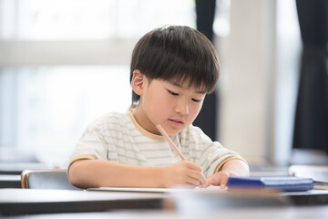 An elementary school boy studying and holding a pencil during class in a classroom