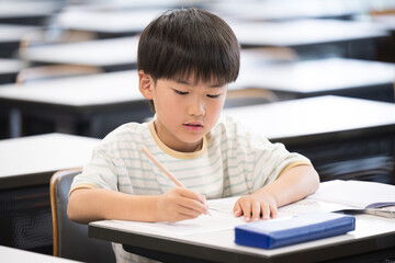 An elementary school boy studying and holding a pencil during class in a classroom