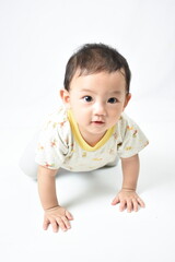 Adorable baby crawling on a white background, looking curiously at the camera with big, bright eyes and a sweet smile. Dressed in a cute patterned shirt, showcasing innocence and curiosity.