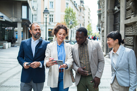 Group of diverse business professionals walking and looking at a smartphone on a city street