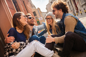 Group of friends sitting on street laughing and talking