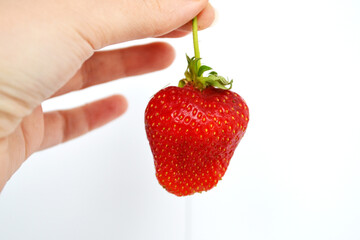 hand is holding a fresh, ripe strawberry. The strawberry is vibrant red in color, with small seeds visible on its surface.  image captures the essence of summer with a delicious strawberry 