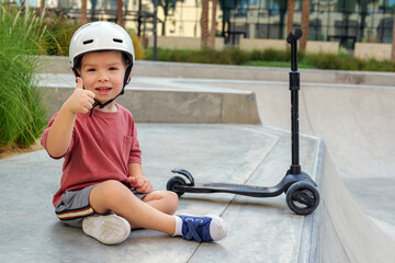 Obraz premium little boy wearing a helmet and with his scooter in a skate park