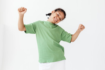 Fototapeta premium Excited young boy in stylish outfit raises arms in celebration against a green background