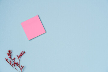 Pink paper note sticker with flower on a blue background. Space for text. Flat lay, top view.