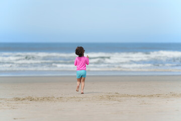 menina de 5 anos correndo sozinha na praia. Sensação de liberdade na infância.