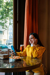 Trendy latin woman using mobile while having a beer in modern bar.
