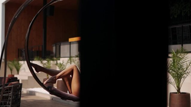 Lovely model with slim body shape laying down, sunbathing on swing and posing in bikini at summer pool party. Dark hair model in swimsuit enjoys sun on vacation in luxury beach club.