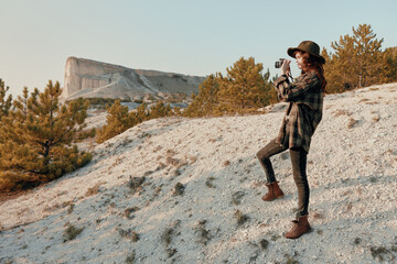 Woman in hat and plaid shirt standing on hilltop with mountain in background