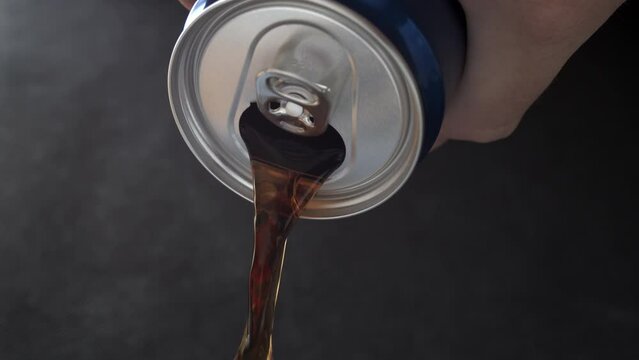 Opened soda can, dark liquid pours from the can.