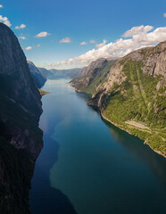 A breathtaking aerial view of a deep, narrow fjord in Norway, with steep cliffs on both sides and a bright blue sky above. Kjerag, Lysebotn, Lysefjorden, Norway
