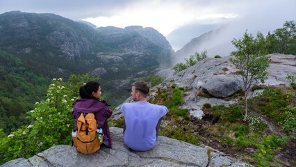 Two people sit on a rocky mountaintop overlooking a valley shrouded in mist. Preikestolen, Norway