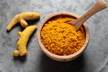 Turmeric powder in wooden bowl and dried turmeric root on grey background close-up top view
