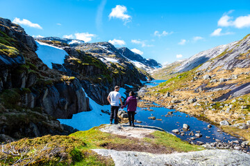 A couple stands on a rocky outcrop overlooking a serene glacial lake in Norway. Kjeragbolten Norway © Fokke Baarssen