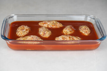 Preparing meat or cutlets patties with rice, baking them in a dish with tomato sauce. Home cooking, traditional recipes, and culinary preparation.