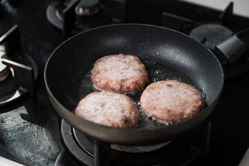 Meatballs or small meat patties cutlets sizzling in oil while frying in a pan on the stove. Concept of home cooking, traditional recipes, and culinary preparation