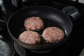 Meatballs or small meat patties cutlets sizzling in oil while frying in a pan on the stove. Concept of home cooking, traditional recipes, and culinary preparation