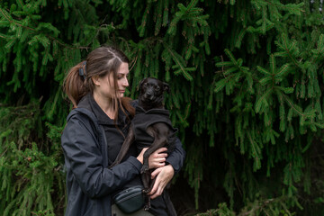 Portrait of a young beautiful woman and her black small dog outdoors, Wearing black clothes