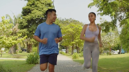 Tracking shot of cheerful intercultural sportspeople having jog when training in sunny park