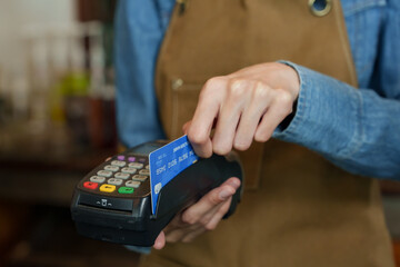 Hand guiding a blue credit card into a portable card machine held by barista, with a clear view of the keypad and barista&rsquo;s apron. Cashless payments. Small family business