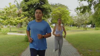 Tracking slowmo shot of biracial sporty couple jogging in park when training for marathon