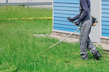 A man is cutting grass with a lawn mower. The grass is short and the man is wearing a grey jumpsuit