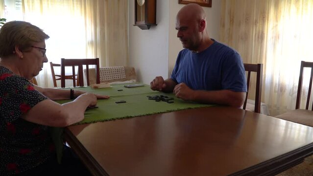 A man with a senior woman playing dominoes in a table at home.