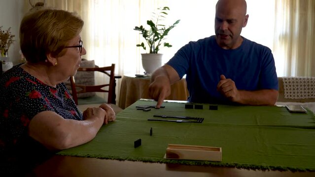 A man with a senior woman playing dominoes in a table at home.