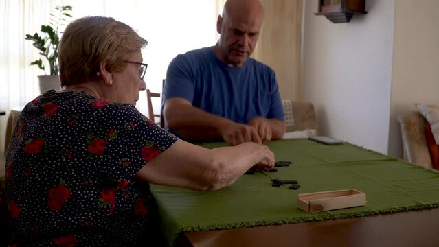 A man with a senior woman playing dominoes in a table at home.