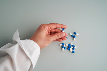 A hand holds a white and blue pill on a blue background.