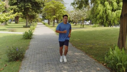 Tracking shot of young Asian sportsman exercising for marathon when visiting local park at weekend